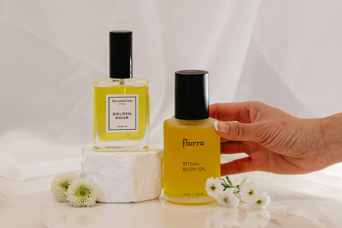 Two bottles of body oil with a hand holding one, on a light background.